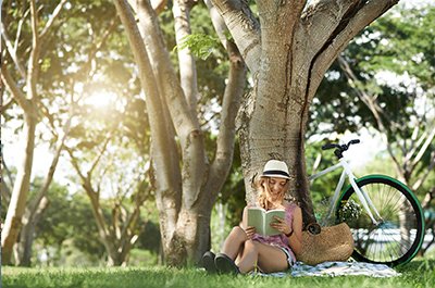 Junge Frau liest Buch unter Baum im Park